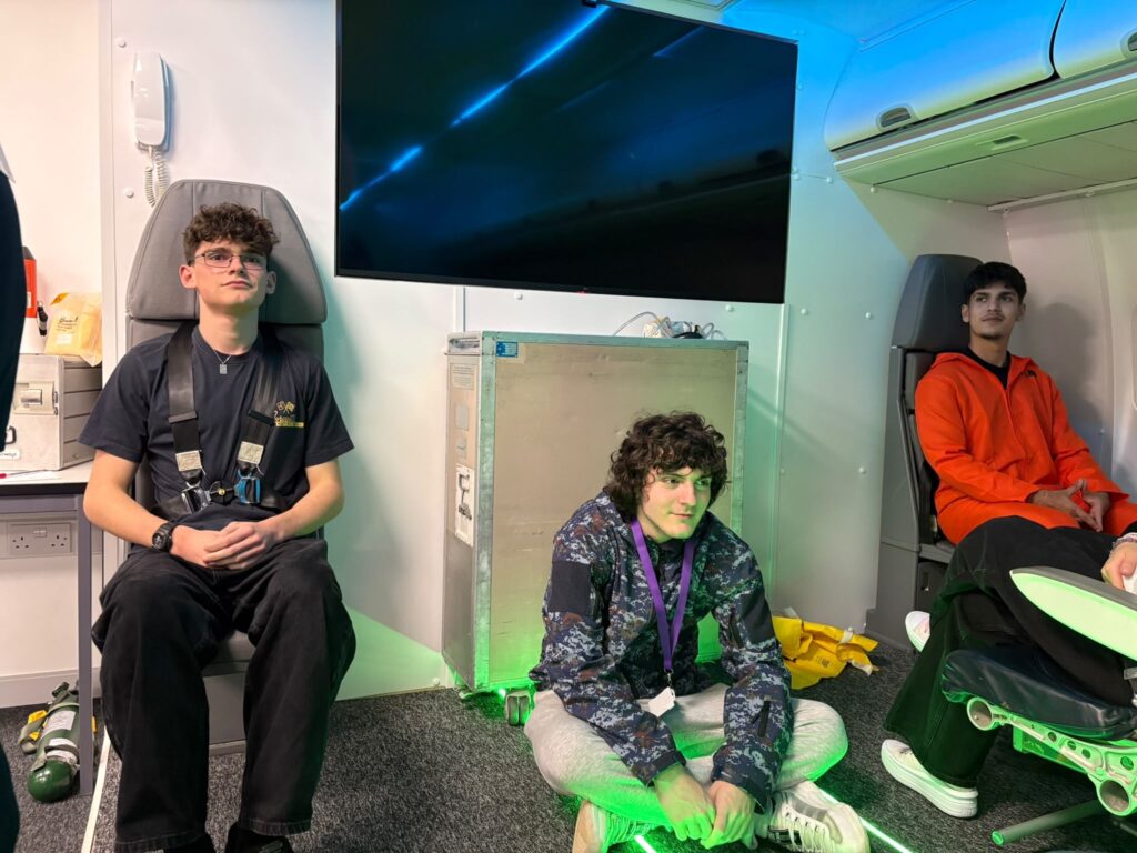 Three students in cabin crew jump seats with their harnesses fastened.
